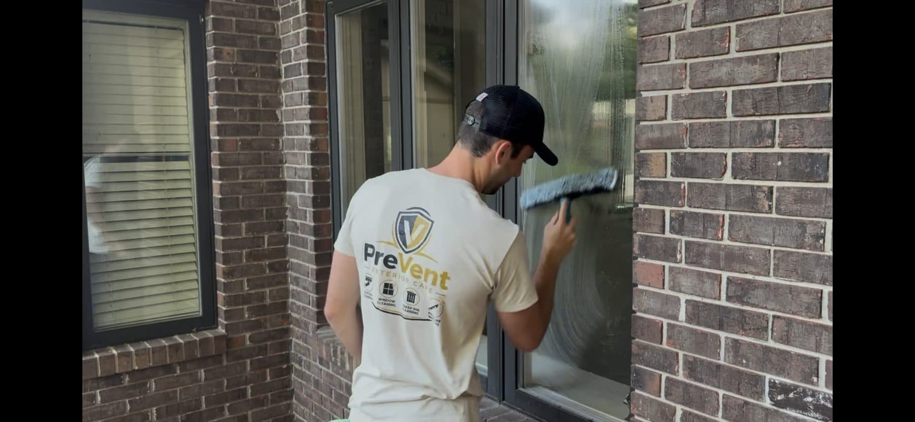 Squeegeeing a window on a brick home in the Shoals, PreVent shirt on